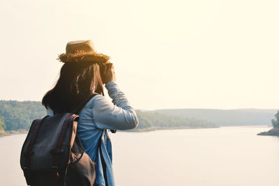 Rear view of woman photographing on landscape against clear sky