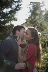 Young couple kissing against trees and plants