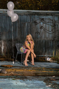 Portrait of woman sitting on chair against retaining wall