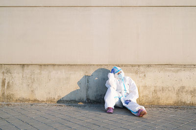 Female nurse sitting with head in hands on footpath against wall