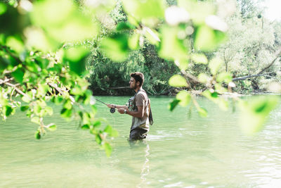 Side view of male fisherman throwing fishing rod into a mountain river