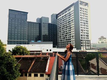 Side view of woman standing against buildings in city