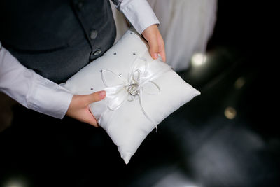Midsection of bridegroom holding wedding ring on pillow