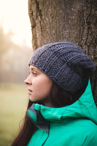 Pleasant and pretty brunette in a winter jacket and knitted hat is looking at her friends