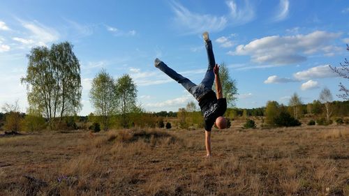Rear view of man doing handstand on grassy field against blue sky