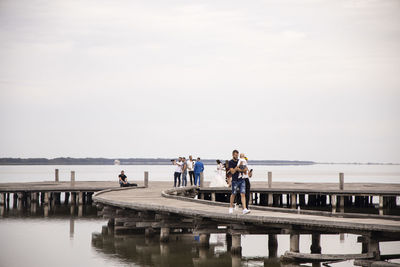 People on pier over sea against sky