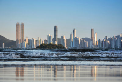 Modern buildings in city by the sea against clear sky