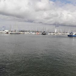 Boats moored at harbor against cloudy sky