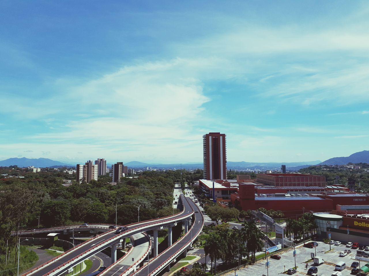 architecture, built structure, building exterior, city, sky, skyscraper, cityscape, high angle view, transportation, cloud - sky, modern, outdoors, development, tree, day, bridge - man made structure, no people, travel destinations, road, city life, growth, mountain, urban skyline, nature