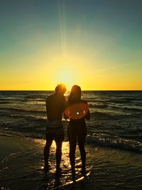 Rear view of friends standing on beach against sky during sunset