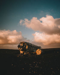 Abandoned airplane on field against cloudy sky during sunset