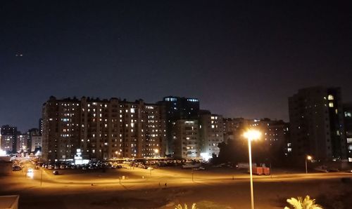 Illuminated buildings by street against sky at night