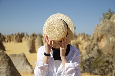 Woman covering face with hat against sky