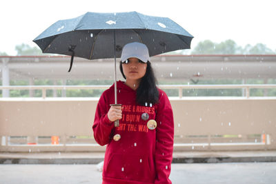 Young woman holding umbrella while standing on road during rainfall in city