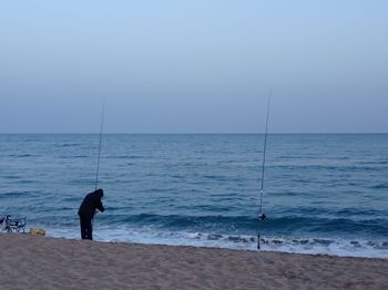 Silhouette man standing on the beach fishing 