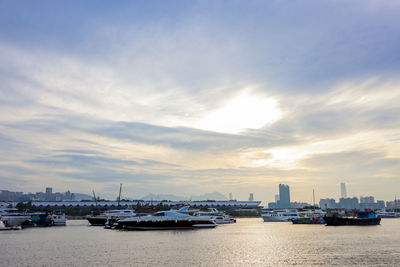 Boats moored on sea by buildings against sky during sunset