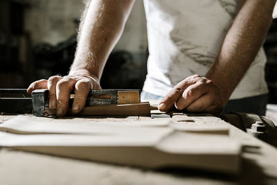 Crop male woodworker standing at old workbench and working with lumber details in grungy workshop