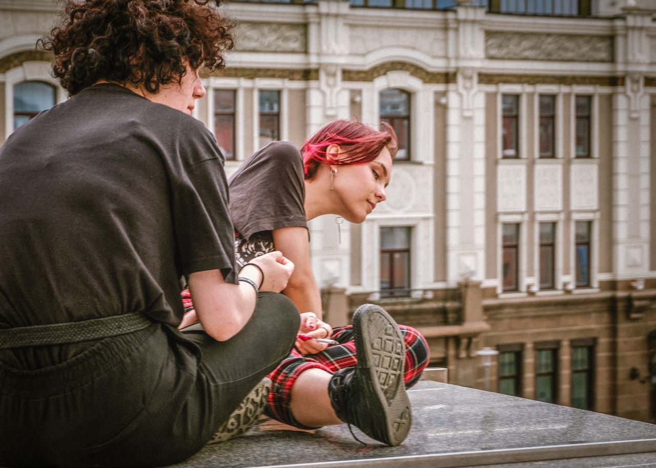 two people, architecture, young adult, adult, young women, rear view, women, building exterior, city, focus on foreground, togetherness, day, love, built structure, casual clothing, people, young men, sitting, hairstyle, couple - relationship, teenager