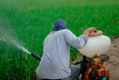 Rear view of man spraying pesticide on agricultural field