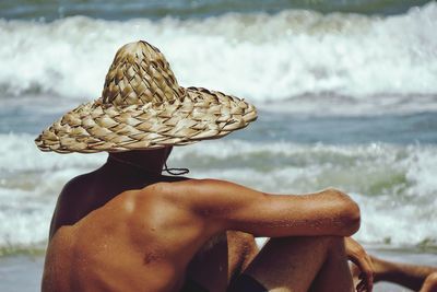 Rear view of man wearing hat at beach against sky