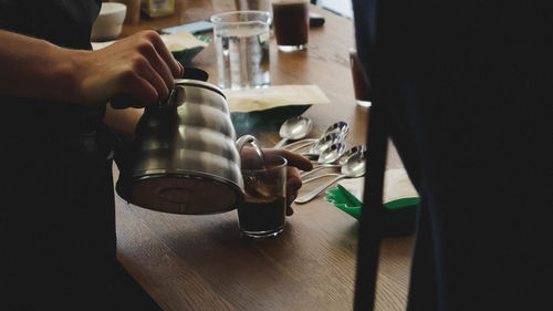 Midsection of man pouring coffee in glass on wooden table