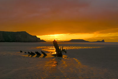 Silhouette person on beach against sky during sunset