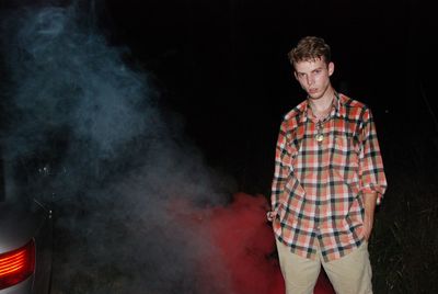 Young man standing by smoke on field at night