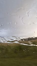 Close-up of wet glass against sky