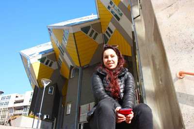 Portrait of smiling young woman sitting against sky