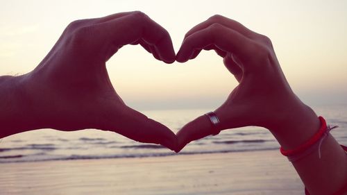 Close-up of hands making heart shape against sky during sunset