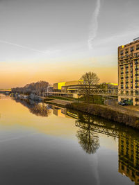 Bridge over river by buildings against sky during sunset