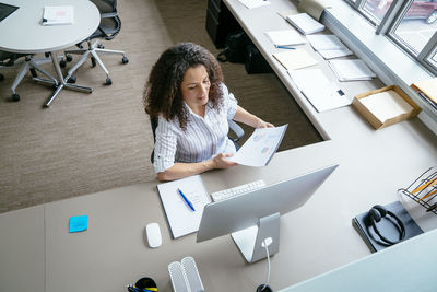 High angle view of businesswoman analyzing reports while sitting at desk in office