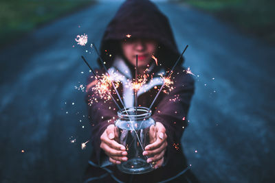 Young woman holding sparklers in jar on road