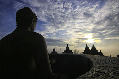 Rear view of silhouette people outside building against sky during sunset