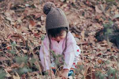 Cute baby girl crouching and playing with leaves during winter