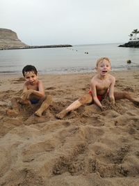 Portrait of cute siblings playing on sand at beach