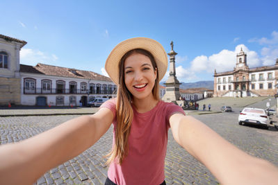 Portrait of young woman wearing hat standing against sky