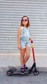 Full length of girl wearing sunglasses standing on push scooter in city