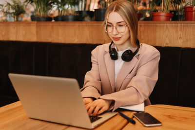 A smiling student wearing glasses and headphones works and studies online using wireless technology