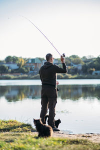 Fisherman with spinning rod and cat near him on nature background. angler man with fishing spinning