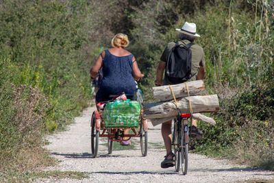 Rear view of man and woman riding bicycles on dirt road
