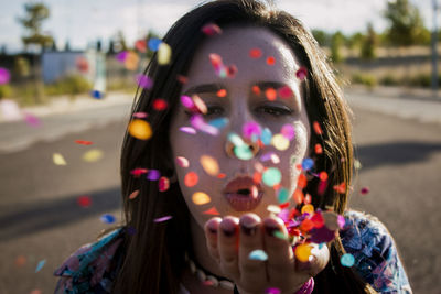 Close-up portrait of young woman blowing confetti