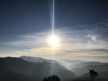 Sunlight streaming through silhouette mountains against sky