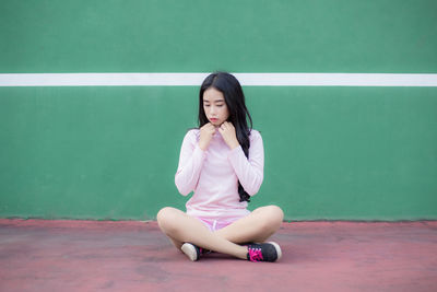 Full length of young woman sitting on court against wall