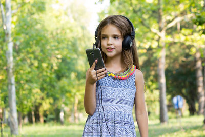 Smiling girl listening music while standing at park