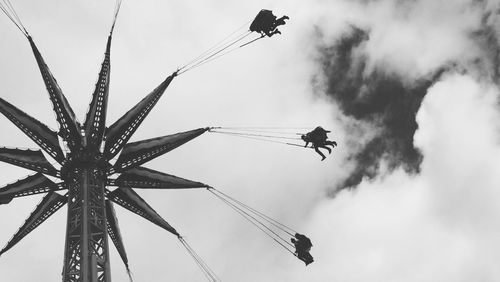 Low angle view of silhouette people enjoying chain swing ride against cloudy sky