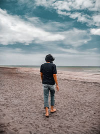 Rear view of man standing on beach against sky