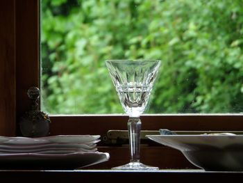 Close-up of glass with plates on table by window