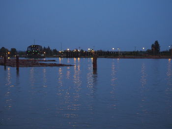 Illuminated buildings by river against sky at night