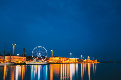 Illuminated ferris wheel by sea against sky at night